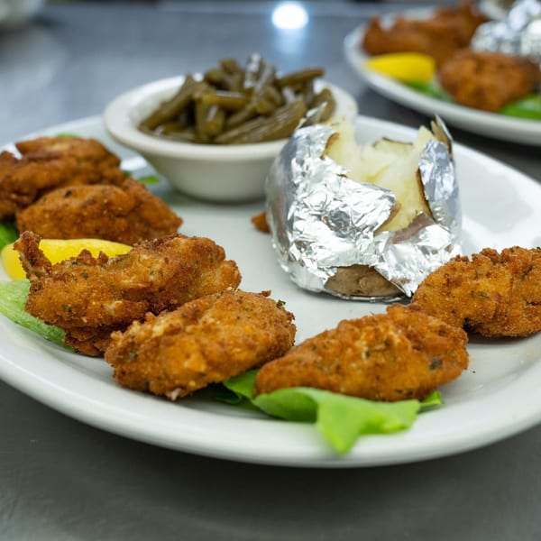 Fried chicken tenders with a baked potato and green beans on a white plate at Colonial Bar & Grill.