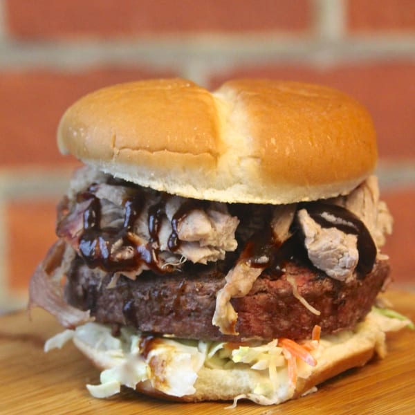 A Colonial Bar & Grill burger with pulled pork, BBQ sauce, and coleslaw on a bun.