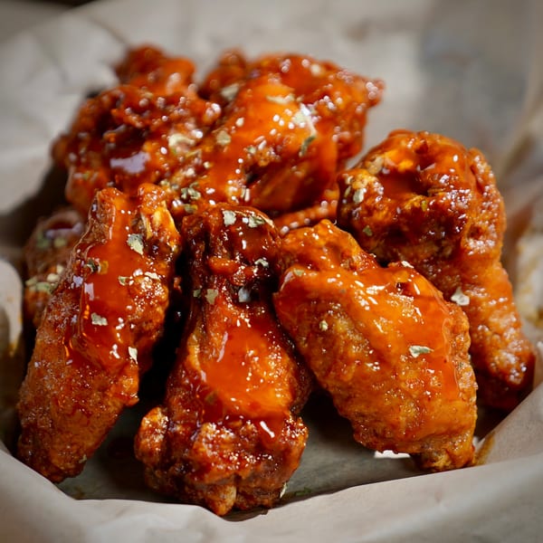 Close-up of Colonial Bar & Grill's chicken wings, coated in a glistening orange sauce with seasoning.
