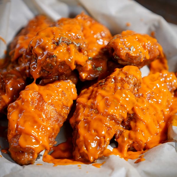 Close-up of Colonial Bar & Grill's buffalo wings, generously coated in bright orange sauce, served in a basket.