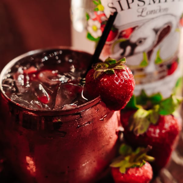 A strawberry cocktail in a copper mug with ice, garnished with a fresh strawberry and a black straw.