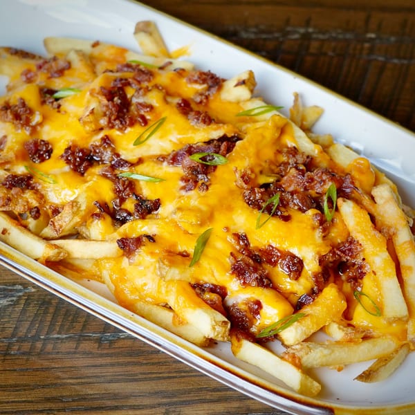 Loaded fries with melted cheddar cheese, crispy bacon bits, and green onions on a white platter.