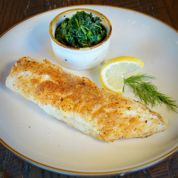 Pan-seared fish fillet with a side of sautéed spinach, lemon wedge, and dill on a white plate.