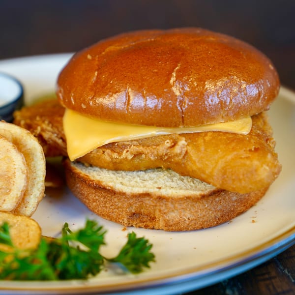 Colonial Bar & Grill's fried fish sandwich with cheese, chips, and parsley on a plate.