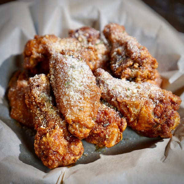 Close-up of crispy fried chicken wings, dusted with parmesan cheese and herbs, served in a paper-lined basket.